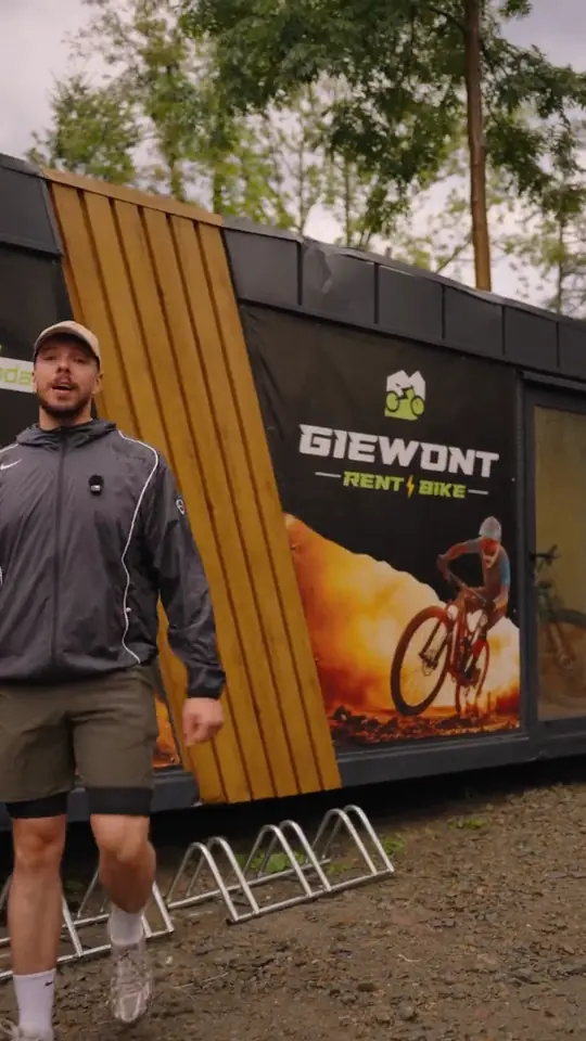 Mężczyzna w czapce idzie przed kontenerem wypożyczalni z logo Giewont Rent Bike, obok stojaki na rowery