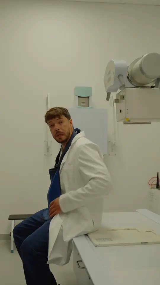 Mężczyzna w białym fartuchu siedzi na stole aparatu RTG w jasnej pracowni