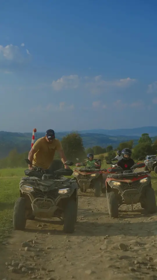Mężczyzna w czapce i musztardowej koszulce przy quadzie, za nim młodzi kierowcy w kaskach na quadach na polnej drodze